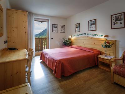 Gemütliches Schlafzimmer mit Holzmöbeln, roter Bettdecke, Balkon und dekorativen Bildern an der Wand.