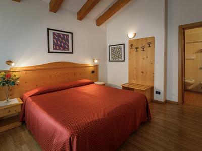 Gemütliches Schlafzimmer mit Holzboden, Doppelbett mit roter Bettdecke und Holzmöbeln.