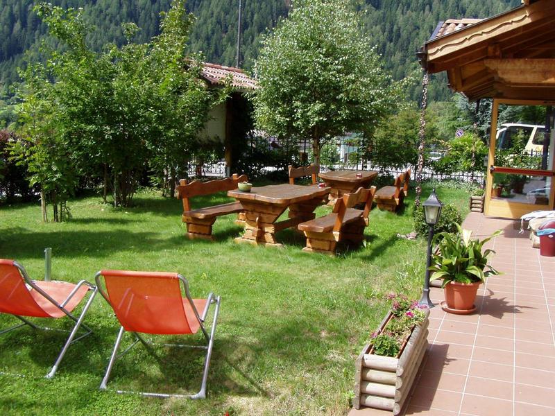 Grüner Garten mit Holzbank, Tisch, roten Gartenstühlen und Topfpflanzen neben Terrasse.