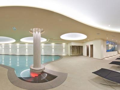 Modernes Hallenbad mit runden Deckenlichtern, weißen Wänden, Säule und schwarzen Liegen.