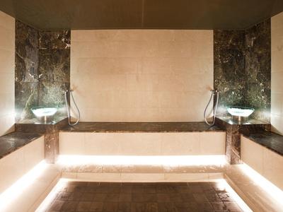 Moderner, beleuchteter Wellnessraum mit dunklem Marmor, Holzbänken und Glaswaschbecken.