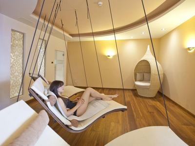 Frau entspannt auf weißem Schwebesessel in modernem, warm beleuchtetem Ruheraum mit Holzfußboden.