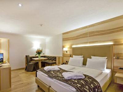 Modernes Hotelzimmer mit Doppelbett, Holzvertäfelung, Sitzecke, Schreibtisch und Fernseher.