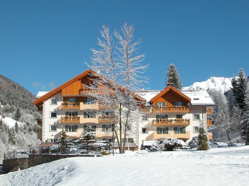 Großes Holzhaus mit Balkonen in schneebedeckter Berglandschaft und klarem blauem Himmel.