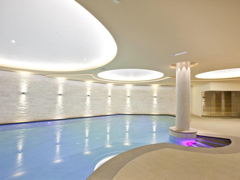 Innenraum eines modernen Schwimmbads mit weißem Mauerwerk, runden Deckenleuchten und integriertem Whirlpool.