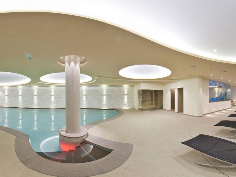 Modernes Hallenbad mit runden Deckenlichtern, weißen Wänden, Säule und schwarzen Liegen.