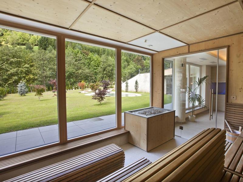 Modernes Saunaraum mit großen Glasfenstern, Holzbänken und Blick auf einen grünen Garten.