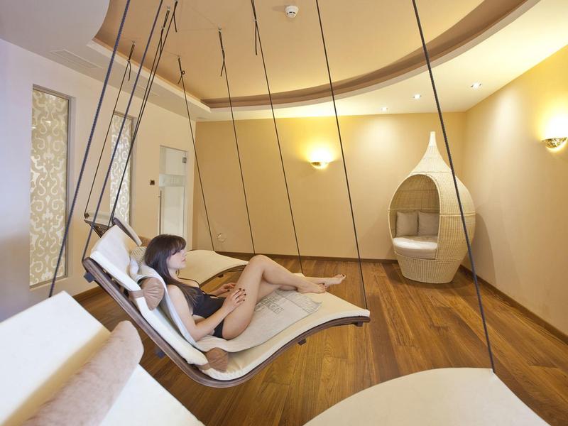 Frau entspannt auf weißem Schwebesessel in modernem, warm beleuchtetem Ruheraum mit Holzfußboden.