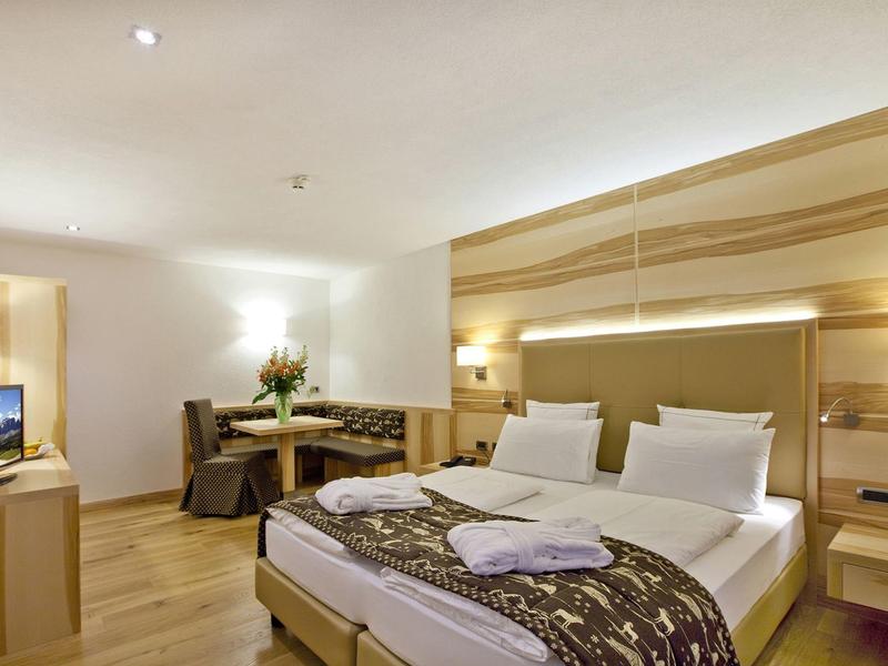 Modernes Hotelzimmer mit Doppelbett, Holzvertäfelung, Sitzecke, Schreibtisch und Fernseher.