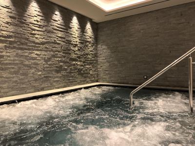 Piscina interior con agua burbujeante, pared de piedra y luces en el techo en un hotel.