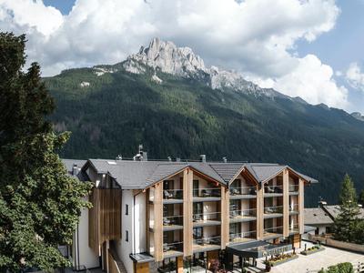 Hotel vor bewaldeten Bergen und einem markanten Felsen unter blauem Himmel mit Wolken