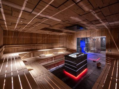 Sauna moderna con bancos de madera, iluminación indirecta y estufa central de piedra con luz roja inferior.