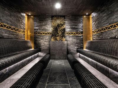 Sala de vapor moderna con azulejos oscuros y detalles dorados en las paredes.