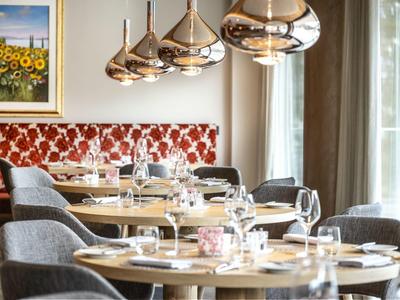 Elegantes Restaurant mit runden Tischen, grauen Stühlen und goldfarbenen Hängelampen.