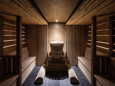 Holzsauna mit zwei Liegen und einem zentralen Ofen unter warmem Licht.