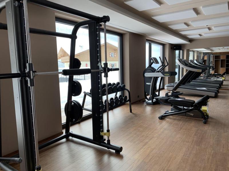 Hell beleuchteter Fitnessraum mit Kraftstation, Kurzhanteln und Laufbändern auf Holzfußboden.