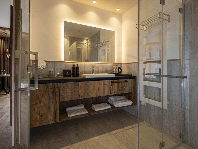 Modernes Badezimmer mit Holzmöbeln, Waschtisch, Spiegel und begehbarer Glasdusche.