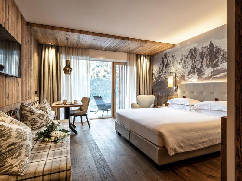 Gemütliches Hotelzimmer mit großem Bett, Holzvertäfelung und Blick auf einen Balkon.
