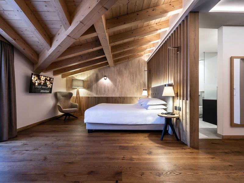 Modernes Hotelzimmer mit Holzboden, Holzbalkendecke und großem Bett unter Dachschräge.