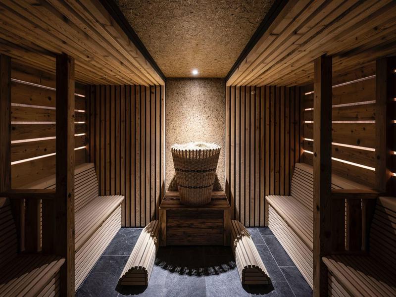 Holzsauna mit zwei Liegen und einem zentralen Ofen unter warmem Licht.