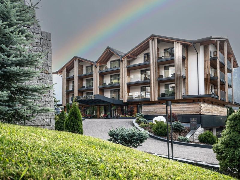 Hotelgebäude in den Bergen mit Regenbogen am Himmel und grüner Umgebung