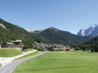 Dorf in gebirgiger Landschaft mit grünen Wiesen, bewaldeten Hügeln und klarem blauem Himmel.