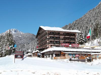 Hotelgebäude im verschneiten Berggebiet mit klar blauem Himmel und Tannenbäumen im Hintergrund.