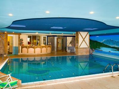 Innenraum mit großem rechteckigem Schwimmbecken, Holztheke, Landschaftswandbild und Liegestühlen.