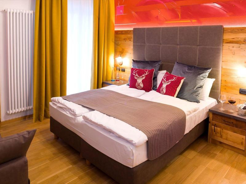 Gemütliches Schlafzimmer mit braunem Bett, Holzfußboden, gelben Vorhängen und roten Akzenten.