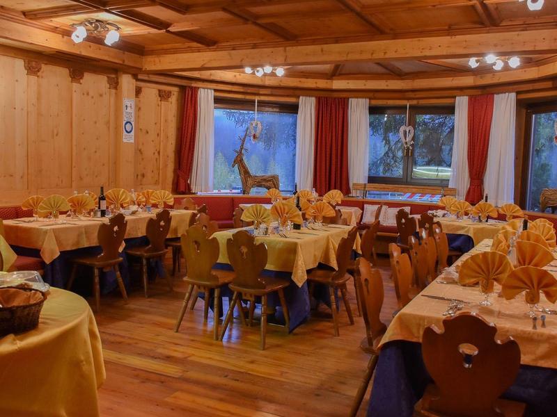 Gemütlicher Gastraum mit Holzdecke, Tischen mit gelben Tischdecken und geschnitzten Holzstühlen.