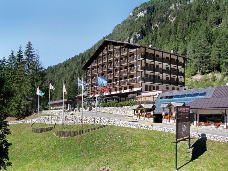 Mehrstöckiges Holzgebäude in Berglandschaft mit grünem Hang und blauem Himmel im Hintergrund.
