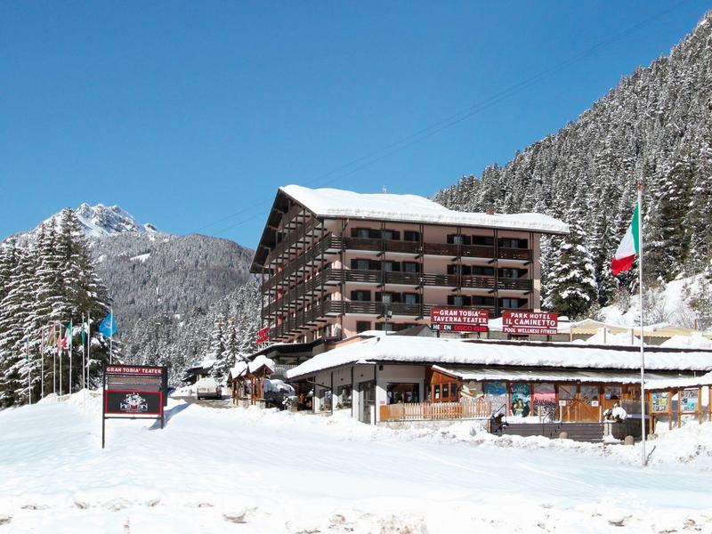 Ein großes Berghotel mit Schnee bedecktem Dach vor verschneiten Bergen und blauem Himmel.