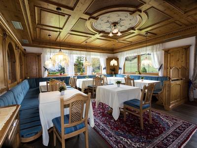 Gemütlicher Raum mit Holzwänden, blauem Ecksofa, weißen Tischen und Teppich in warmem Licht.