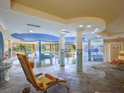 Área de piscina cubierta luminosa con sillas reclinables y grandes ventanas con vista a la terraza.