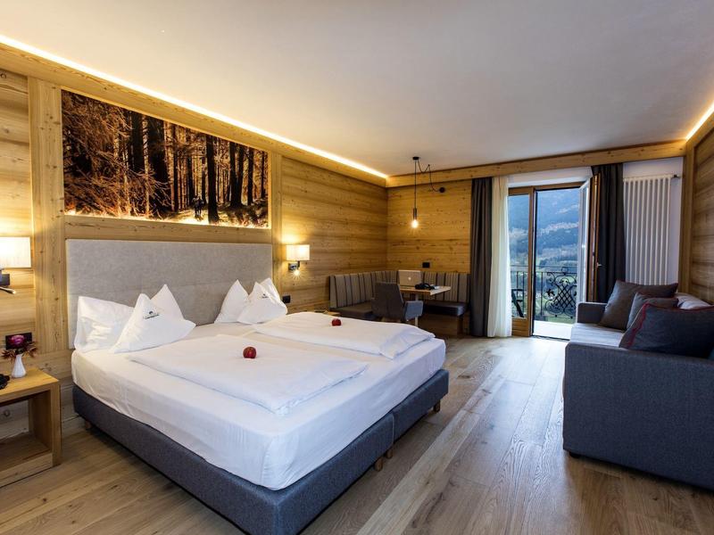 Gemütliches Schlafzimmer mit großem Bett, Holzwänden, Sofa und Zugang zu Balkon mit Bergblick.