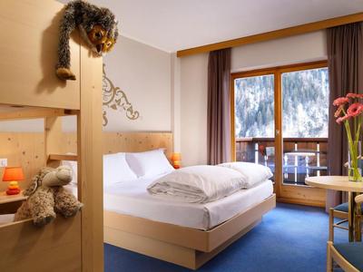 Gemütliches Schlafzimmer mit Holzmöbeln, blauem Teppich und Balkon mit Bergblick.