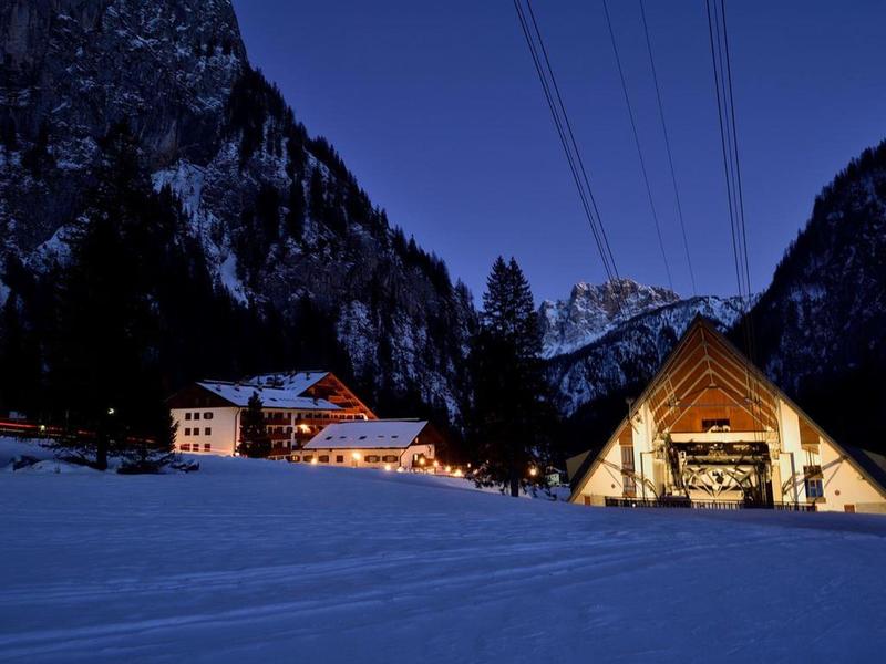 Winterliche Berglandschaft mit schneebedeckten Hütten und beleuchteten Häusern bei Nacht.