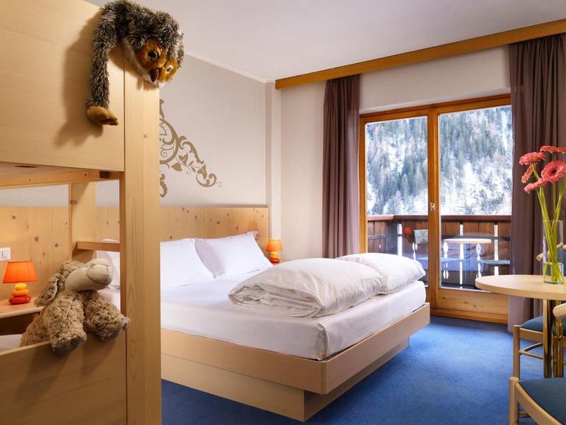 Gemütliches Schlafzimmer mit Holzmöbeln, blauem Teppich und Balkon mit Bergblick.