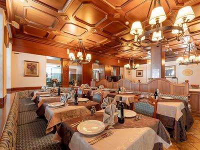 Restaurant mit gedeckten Tischen, Holzmöbeln, verzierter Decke und warmem Licht.