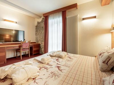 Helles Schlafzimmer mit Doppelbett, Musterbettwäsche, Holzmöbeln und großem Fenster mit Vorhängen.