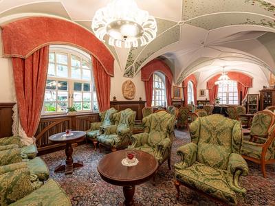 Innenraum mit eleganten grünen Sesseln, Holztischen, roten Vorhängen und gewölbter Decke in warmem Licht.