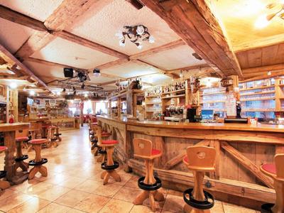 Große, rustikale Bar mit Holzbalken, Hockern und warmem Licht in gemütlicher Atmosphäre.