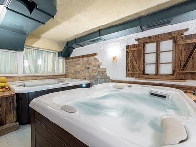 Innenraum mit zwei Whirlpools, Holzverkleidung, rustikalen Fensterläden und gemauerter Wand.