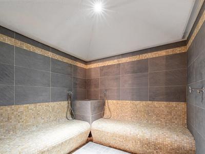 Moderne Sauna mit grauen und beigen Fliesen, zwei Sitzbänken und Deckenbeleuchtung.
