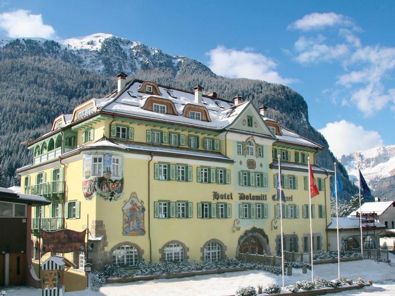 Gelbes Hotel mit verschneitem Dach vor Bergen und blauem Himmel im Winter.