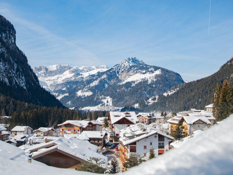 Dorf im Tal mit schneebedeckten Häusern, Bergen rechts und links, schneebedeckter Bergspitze im Hintergrund.
