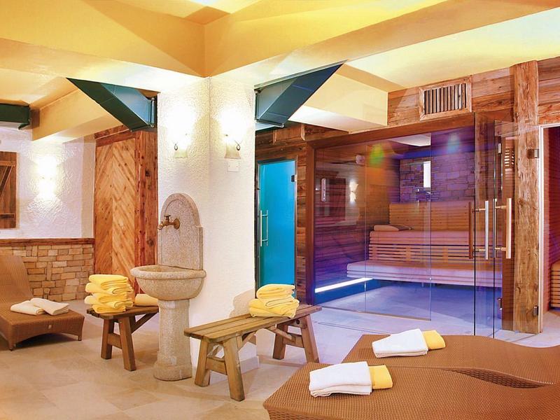 Innenraum eines Wellnessbereichs mit Holzmöbeln, Sauna, Sitzliegen und warmem Licht.