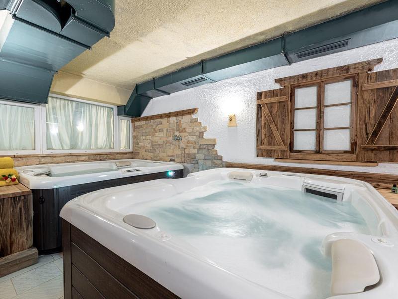 Innenraum mit zwei Whirlpools, Holzverkleidung, rustikalen Fensterläden und gemauerter Wand.