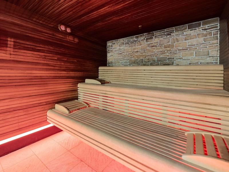 Innenraum einer Holzsauna mit gestuften Holzsitzen und heller Steinwand im Hintergrund.