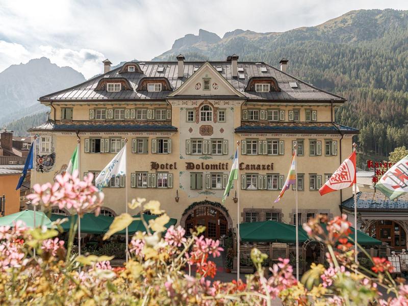 Altes dreistöckiges Hotel mit gelber Fassade und Holzbalkonen vor bewaldetem Bergpanorama.